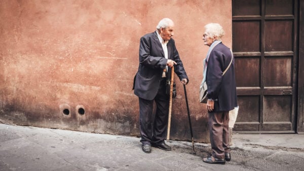 Two elderly people standing next to a lime-washed wall on a cobble road; Researches Unveil the Maximum Age Humans Can Live To