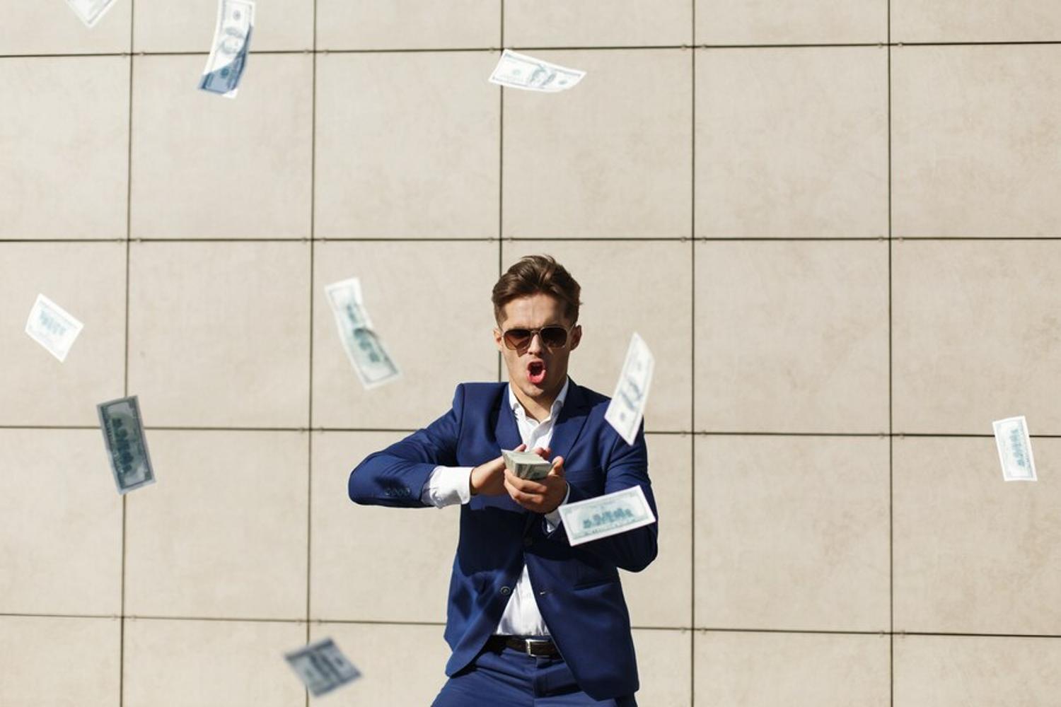 A wealthy man flying several $100 bills in the air